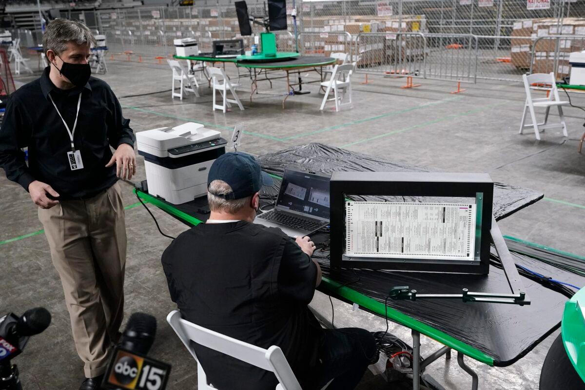 Doug Logan, left, owner of the Florida-based consultancy Cyber Ninjas, talks about overseeing a 2020 election ballot audit ordered by the Republican-led Arizona Senate at the Arizona Veterans Memorial Coliseum, as a Cyber Ninjas IT technician demonstrates a ballot scan during a news conference, in Phoenix, on April 22, 2021. (Ross D. Franklin/AP Photo)