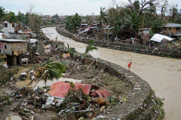 A man stands beside damaged homes along a swollen river due to Typhoon Rai in Talisay, Cebu Province, central Philippines, on Dec. 17, 2021. (Jay Labra/AP Photo)