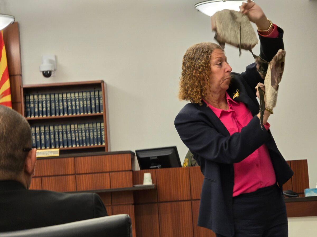 Defense co-counsel Kathy Lowthorpe holds a pair of "carpet booties" during the trial of George Alan Kelly, on April 11, 2024. (Allan Stein/The Epoch Times)