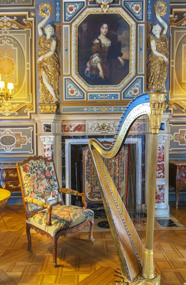 The Grand Salon represents the grandeur of French aristocratic life. At the heart of the room stands a gilded harp and a floral velvet chair. An elegant fireplace is adorned with intricate plasterwork, floral motifs, and colored marble. Above the fireplace, a family portrait gazes upon the room, framed by gilded bas-relief sculptures. (Yuri Turkov/Shutterstock)