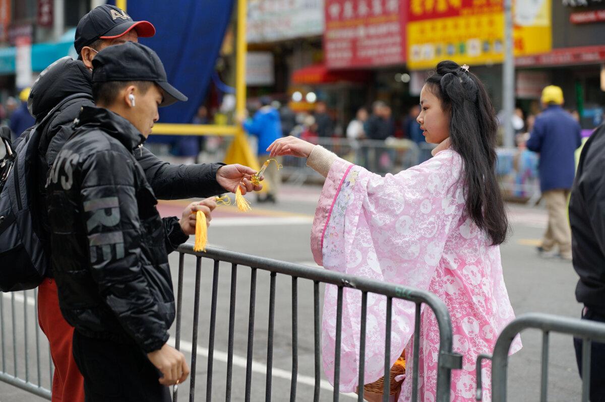 A Falun Gong practitioner hands out souvenirs at a parade calling for an end to the persecution in China of their faith, in the Flushing neighborhood of Queens, New York, on April 21, 2024. (Chung I Ho/The Epoch Times)